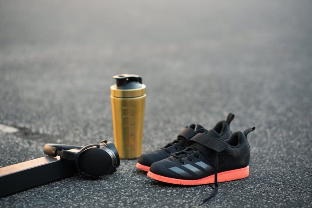 Contemporary sports equipment representing plastic bottle near wireless headset and stylish footwear on asphalt road